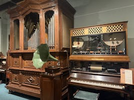 Two wooden cabinet orchestrions side by side, one has a lot of pipes, one has two visible drums. A green gramophone horn sits between them.