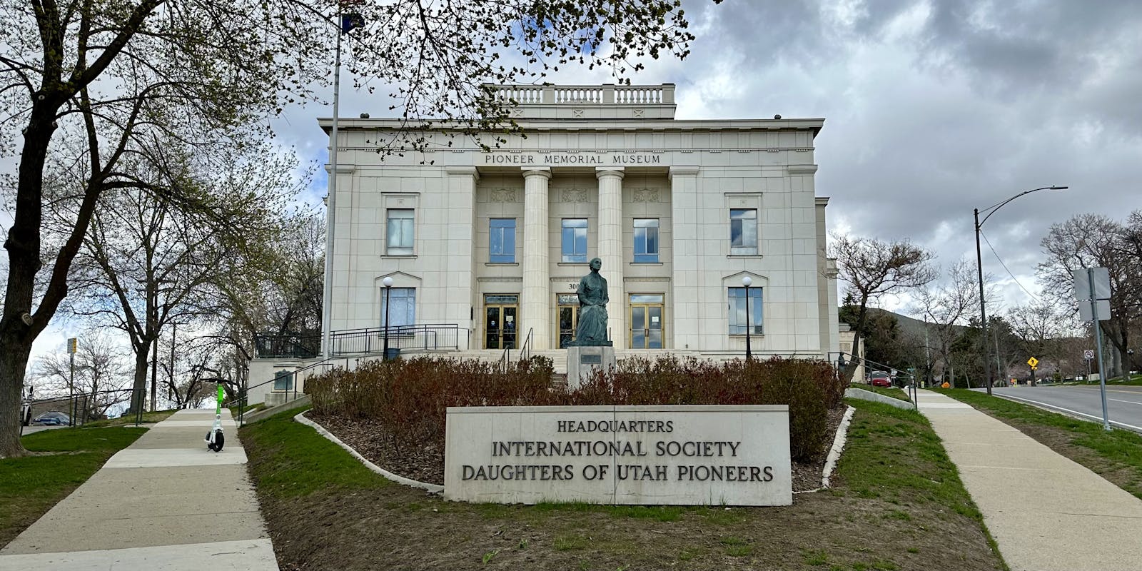 A grand building with Pioneer Memorial Museum written in gold letters along the top, and a plaque in front of it reading Headquarters International Society Daughters of Utah Pioneers