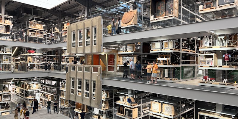 Three levels of glass walkways through the storehouse, museum exhibits everywhere, the facade of a brutalist residential estate hangs near the middle of the photo.