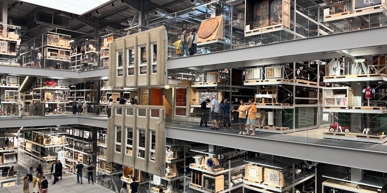 Three levels of glass walkways through the storehouse, museum exhibits everywhere, the facade of a brutalist residential estate hangs near the middle of the photo.